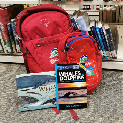 NLPL's whale-watching kit: 2 red backpacks with 2 books about whales; 1 whale and dolphin watching guidebook, and 1 children's picture book